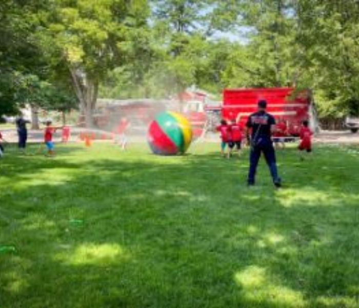 Kids spraying a giant ball with a fire hose at firefighter for a day camp.
